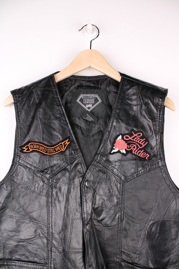 Leather Biker Vest in a black colourway, button up with a v neck collar, and has multiple patches embroidered around the gilet.