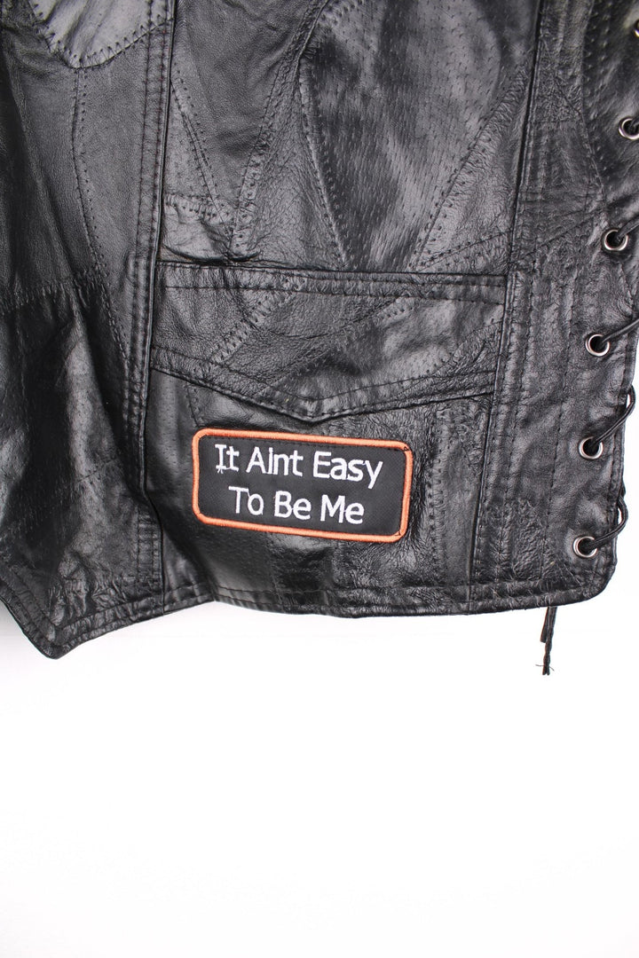 Leather Biker Vest in a black colourway, button up with a v neck collar, and has multiple patches embroidered around the gilet.