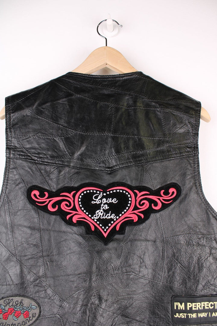 Leather Biker Vest in a black colourway, button up with a v neck collar, and has multiple patches embroidered around the gilet.
