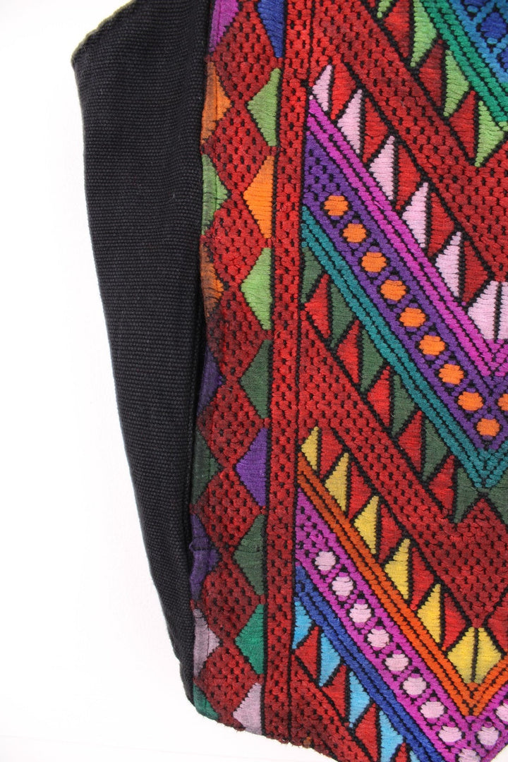 Vintage black vest with multicoloured embroidery, button closure, and a buckled waist adjuster on the back. Handmade in Guatemala.