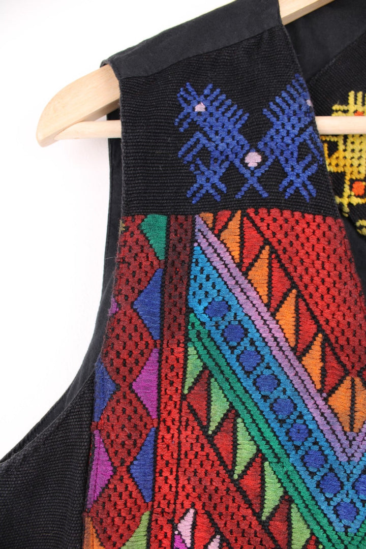 Vintage black vest with multicoloured embroidery, button closure, and a buckled waist adjuster on the back. Handmade in Guatemala.