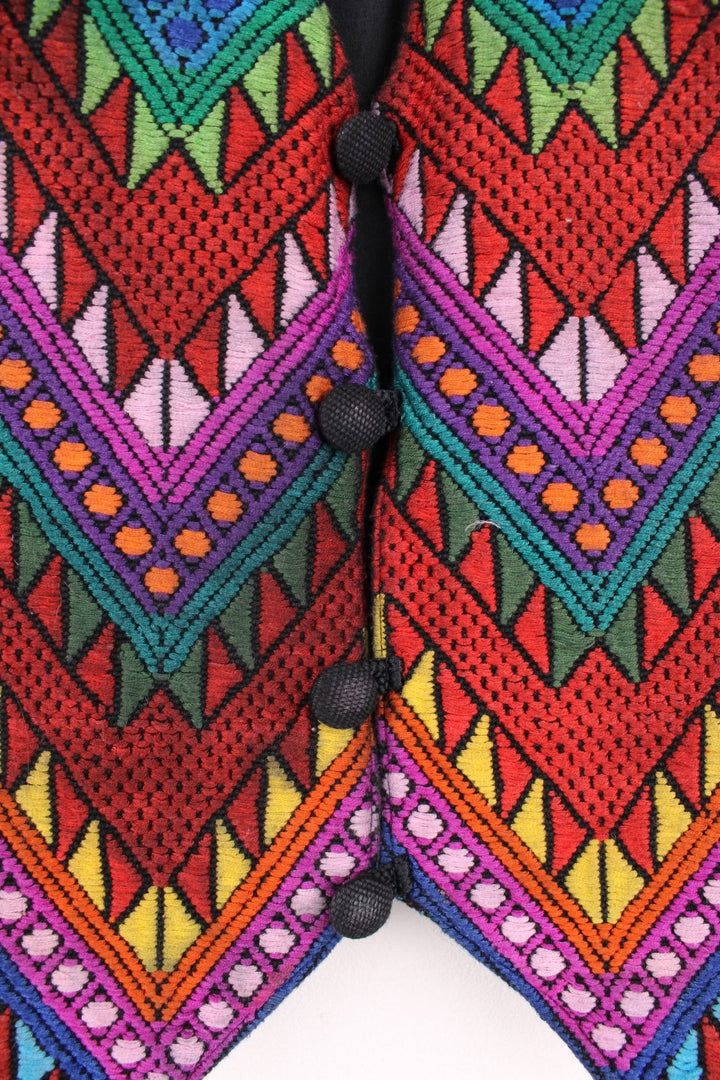 Vintage black vest with multicoloured embroidery, button closure, and a buckled waist adjuster on the back. Handmade in Guatemala.