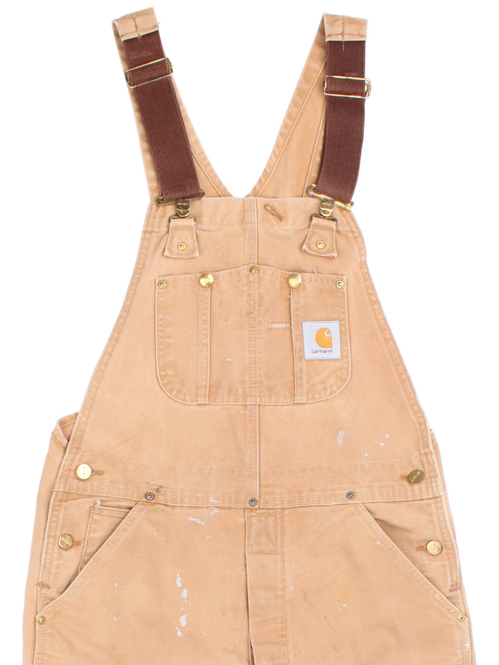 Carhartt Dungarees in tan colourway with multiple pockets, adjustable straps and the logo embroidered on the front.