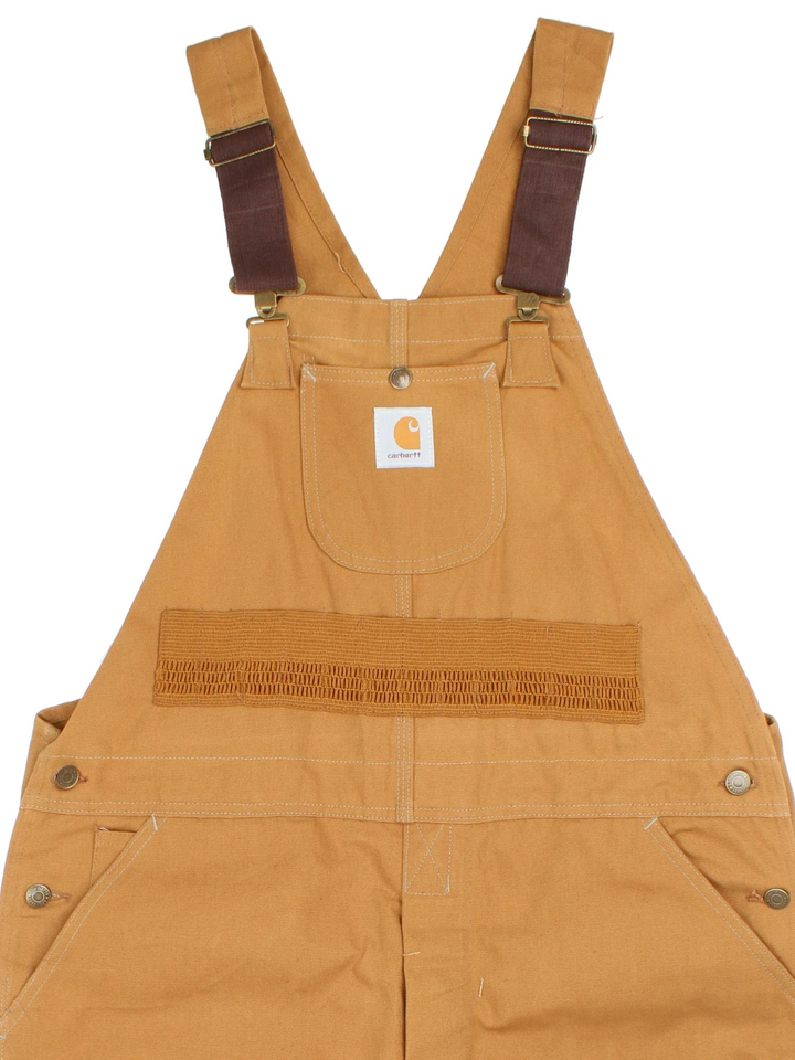 Carhartt Dungarees in tan colourway with multiple pockets, adjustable straps and the logo embroidered on the front.
