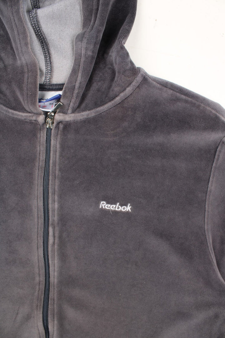 Vintage Reebok Velour Hoodie in a grey colourway. Zip up fastening with side pockets, branding embroidered on front.
