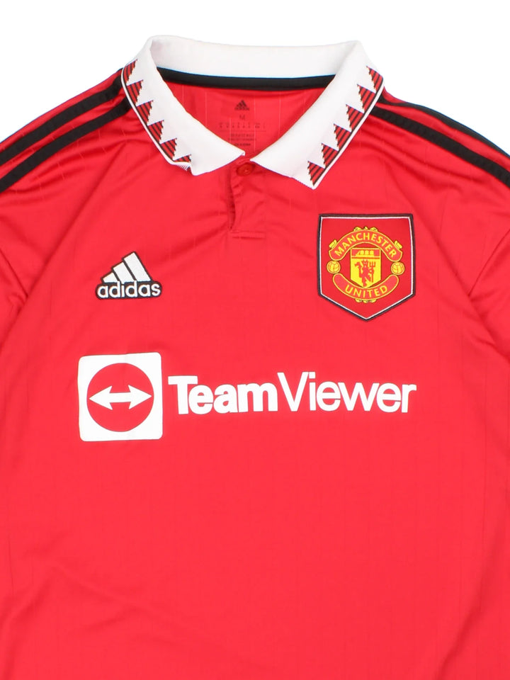 Manchester United 2002/23 Adidas Football Shirt in the red home kit colourway, features printed logos and badge on the front with the classic adidas 3 stripe on the sleeve and button collar.