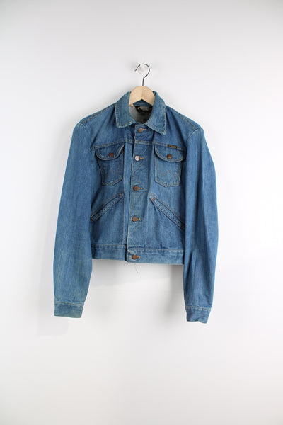Vintage Wrangler Denim Jacket in a blue colourway with brown cross stitching throughout, button up, multiple pockets, and has logo embroidered on the chest.
