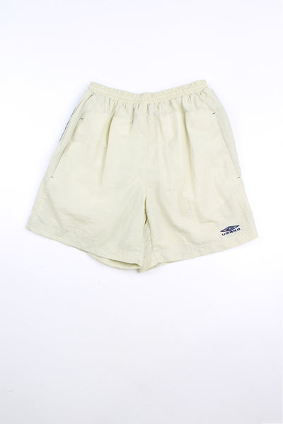 Beige Umbro shorts with elasticated waist and drawstring. Features embroidered logo and blue stripe detail down each leg.