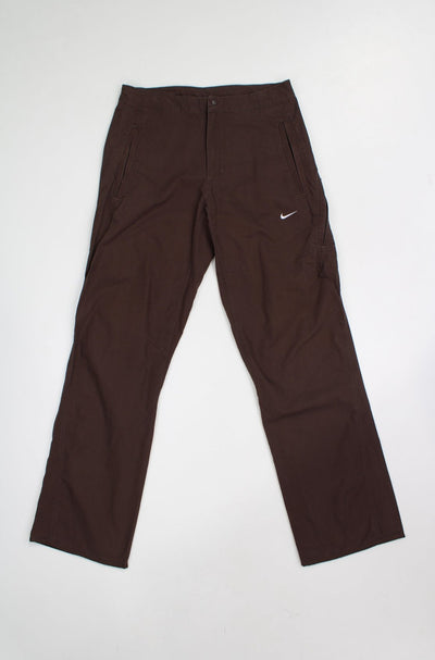 All brown Nike high waisted cotton tech trousers with embroidered logo on the leg and zip up pockets