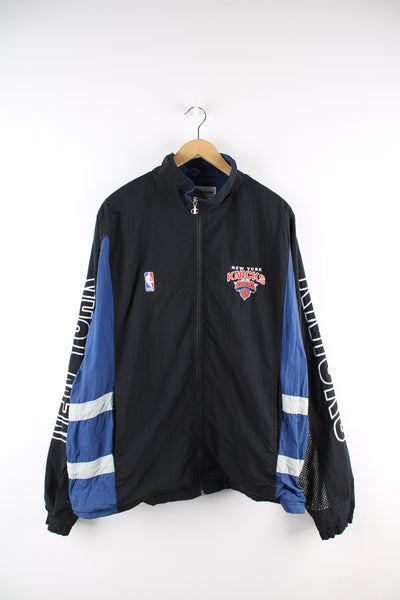Vintage NBA New York Knicks, Champion windbreaker in a black and blue colourway, zip up with side pockets, has embroidered logos on the front, back and sleeves of the jacket. 