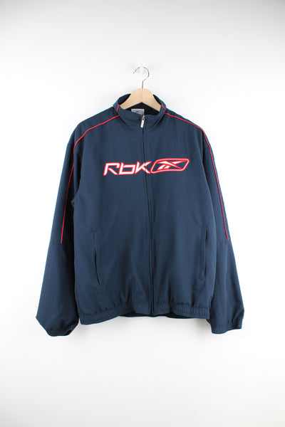 Reebok Tracksuit Jacket in a navy blue and red colourway, zip up, side pockets, and has the logo embroidered on the front and back.