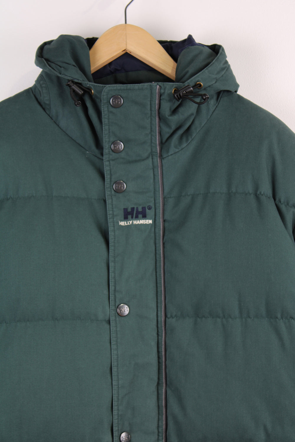 Helly Hansen Down Puffer Jacket in a dark green colourway, zip up, multiple pockets, insulated, hooded and has the logo embroidered on the chest.