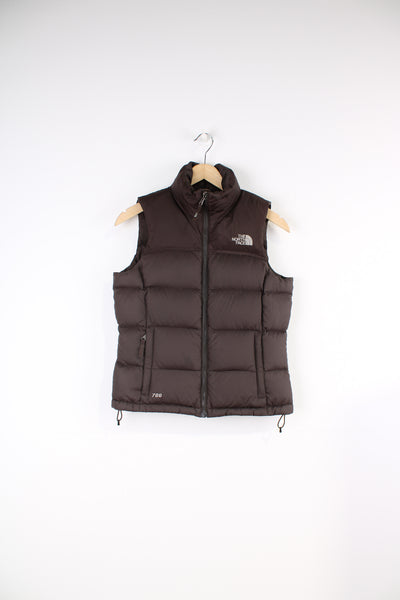 The North Face Face puffer gilet in brown, zip up with side pockets, insulated and has logo embroidered logo on the front and back.