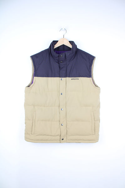 Patagonia Gilet in a tan and dark purple colourway, zip up, side pockets, insulated lining, and has the logo embroidered on the front.