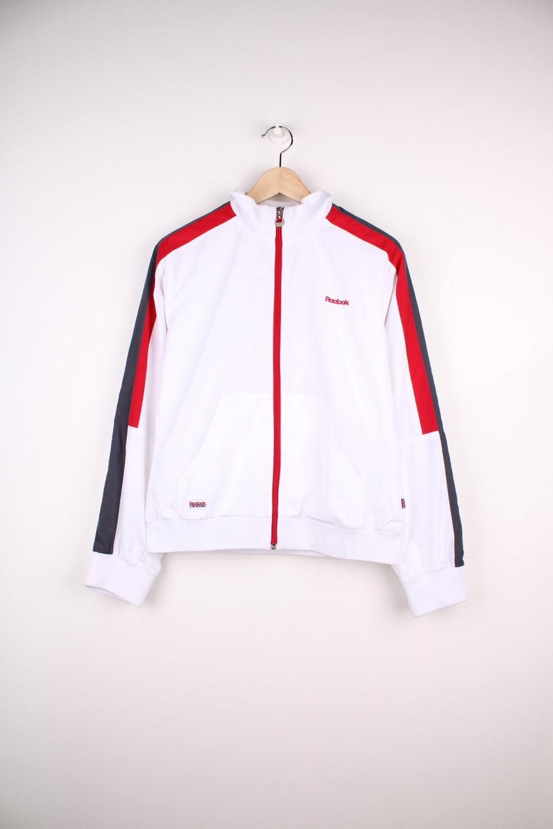 Reebok Classic zip-through tracksuit top in white with red and grey stripes on the sleeves, two pockets and embroidered logos on the chest and back.