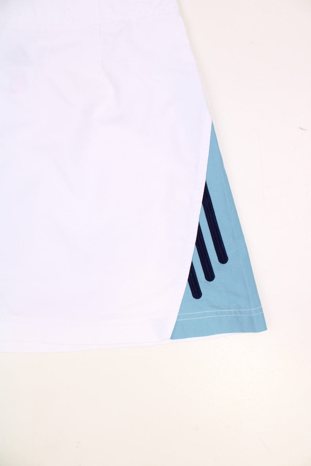 Y2K Adidas mini tennis skirt in white with blue three-stripe design on one side.