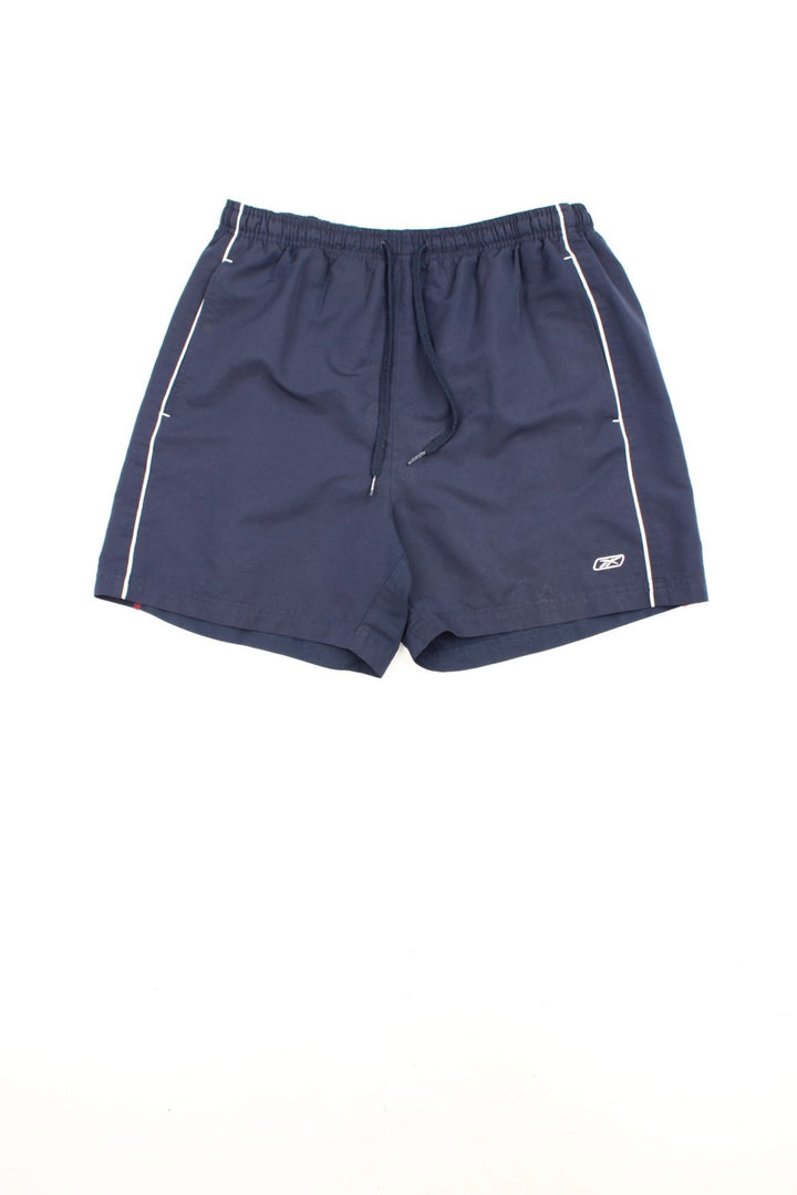 Reebok Shorts in a blue colourway with white stripes going down the sides, has an elasticated waist, mesh netted lining, pockets, and the logo embroidered on the front and down the right side.