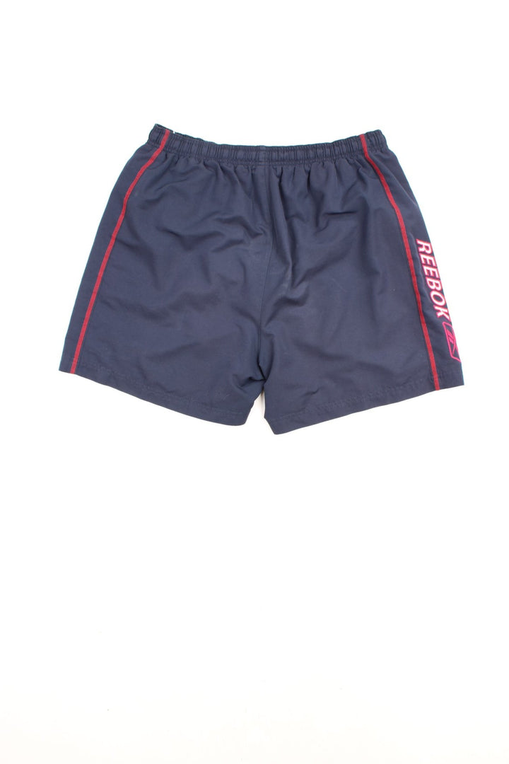Reebok Shorts in a blue colourway with white stripes going down the sides, has an elasticated waist, mesh netted lining, pockets, and the logo embroidered on the front and down the right side.