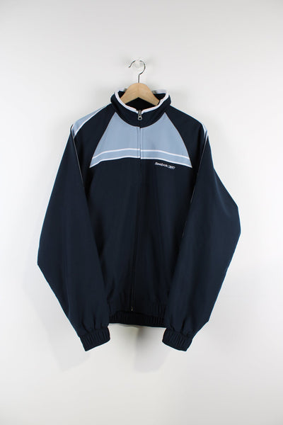 Vintage blue Reebok tracksuit jacket featuring embroidered logo on the chest and blue stripes across the chest and down the arms.