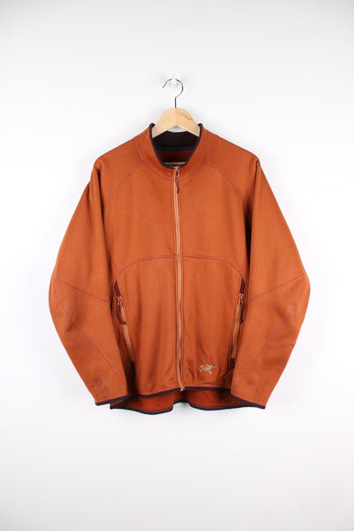 Orange Arcteryx zip through fleece with embroidered logo on the bottom and back, and stitch detailing.