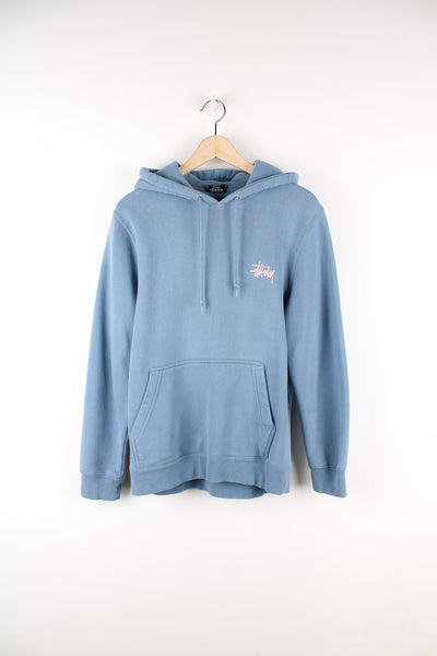 Blue Stussy hoodie featuring pink logo on the chest and graphic print on the back.