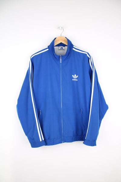Blue Adidas tracksuit top with signature three stripe detail down the sleeves and embroidered logo on the chest.