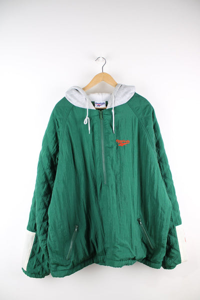 Green Reebok pullover half zip quilted coat. Features embroidered logo on the chest and sleeve, and a zip through hood.