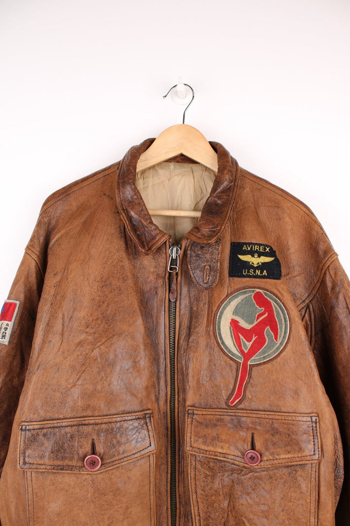 Vintage Avirex Flight Aviator Bomber Jacket in a brown colourway, zip up with side pockets and has badges embroidered on the front alongside the Avirex logo. 