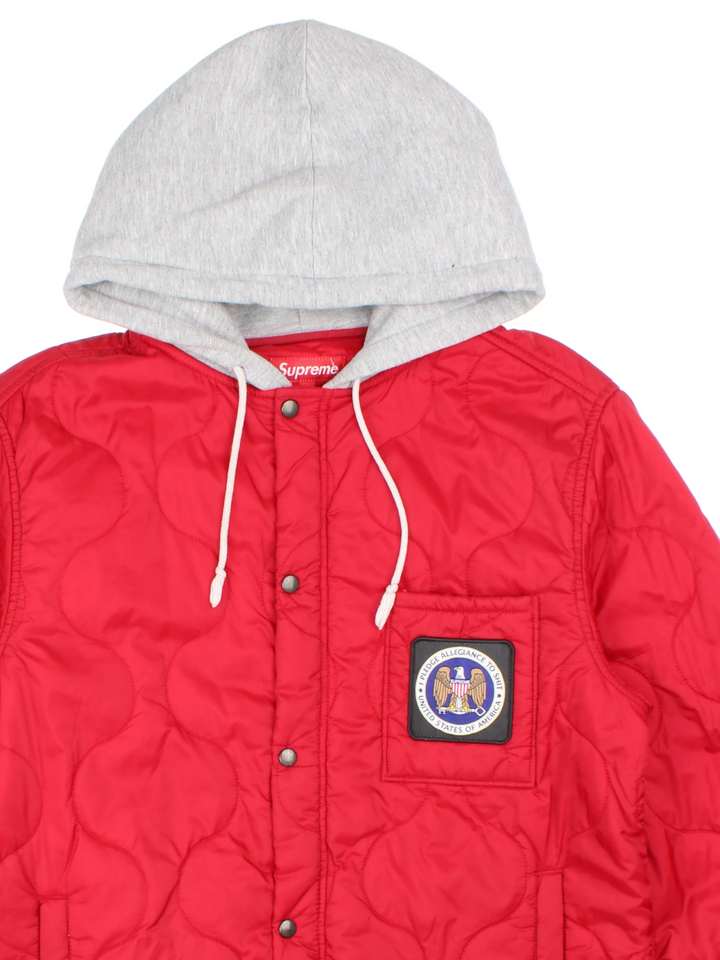 Supreme Quilted Liner Hooded Jacket in a red colourway with a grey cotton hood, "I pledge allegiance to shit, USA" badge embroidered on the front, and has multiple pockets.