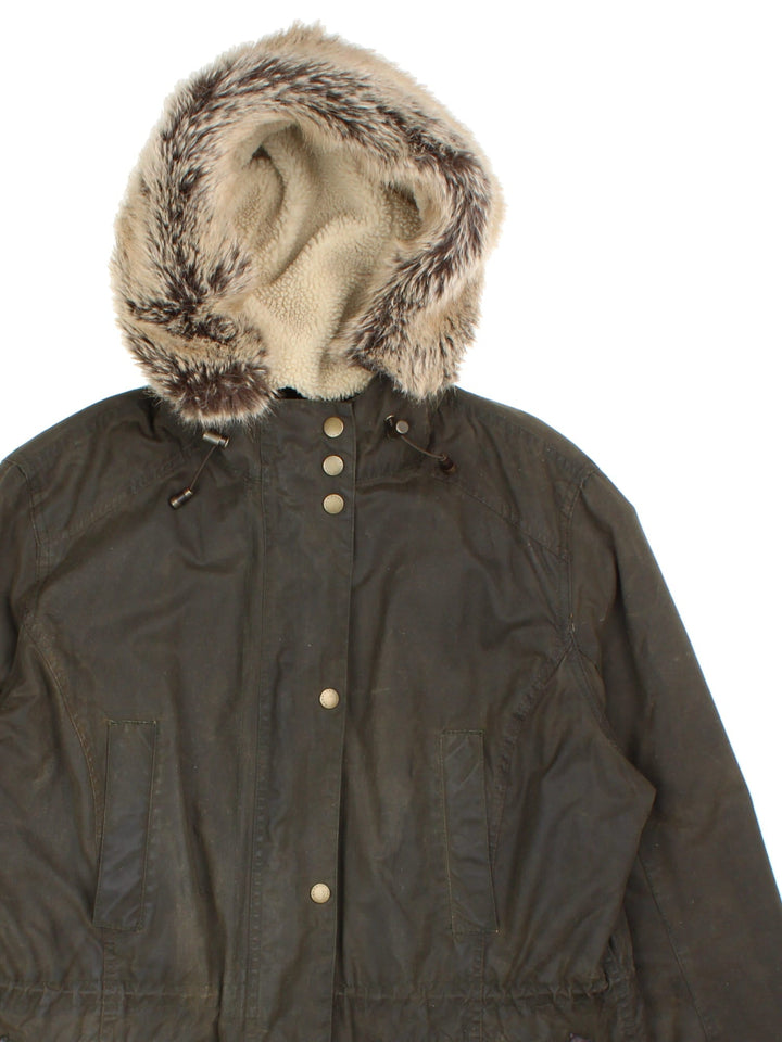 Barbour Kelsall Wax Parka Coat in a green colourway, zips and buttons up, has multiple pockets, hooded with a faux fur and sherpa lining, insulated with a quilted lining, and has the logo embroidered on the front.