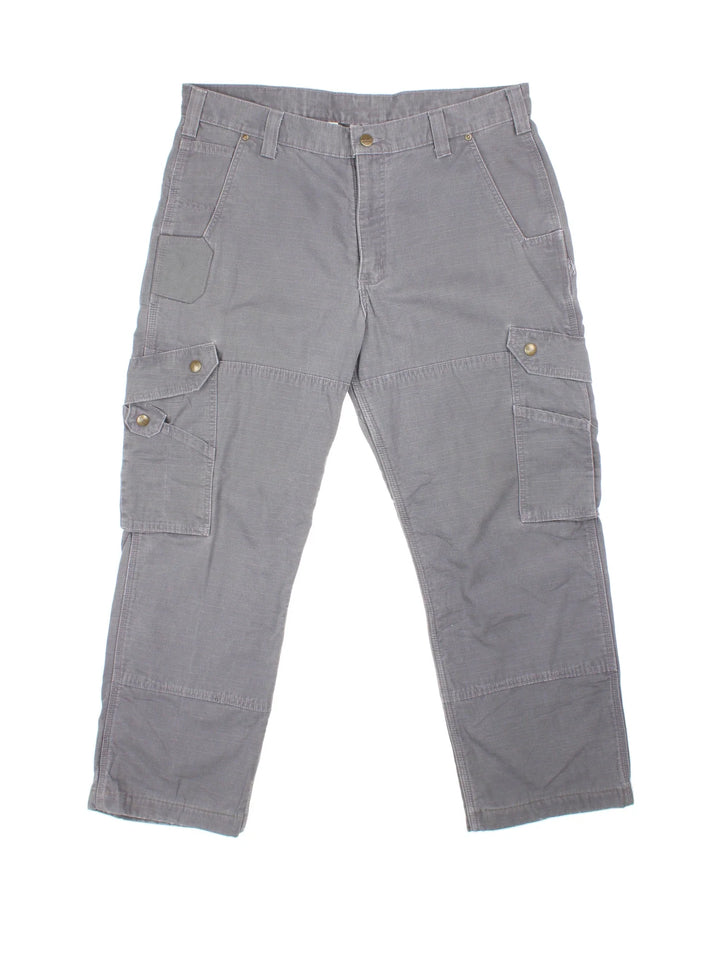 Carhartt Cargo Trousers in a grey colourway with multiple pockets, plaid pattern lining, and the logo embroidered on the back.