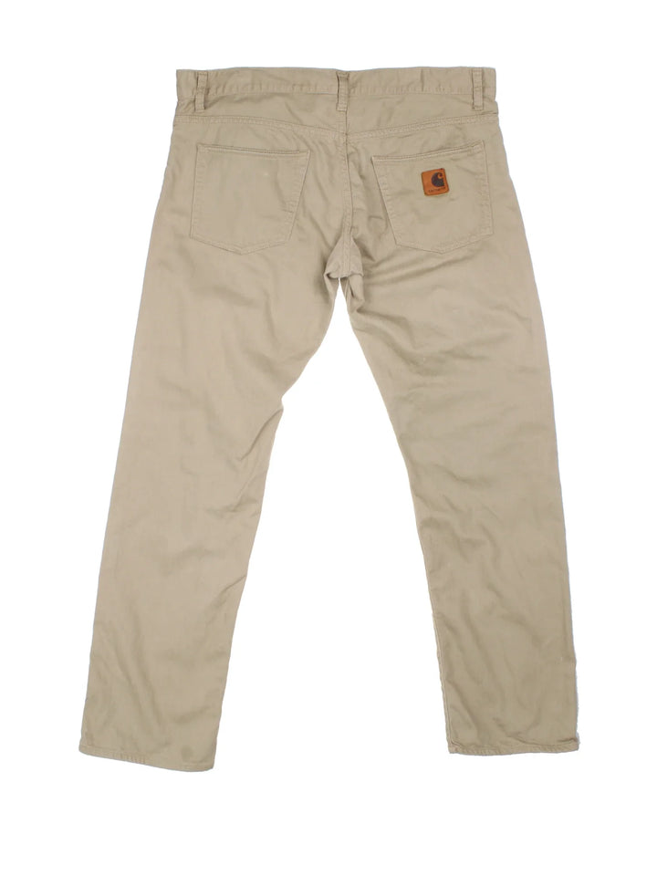 Carhartt Jeans in a tan colourway with multiple pockets and the logo embroidered on the back.