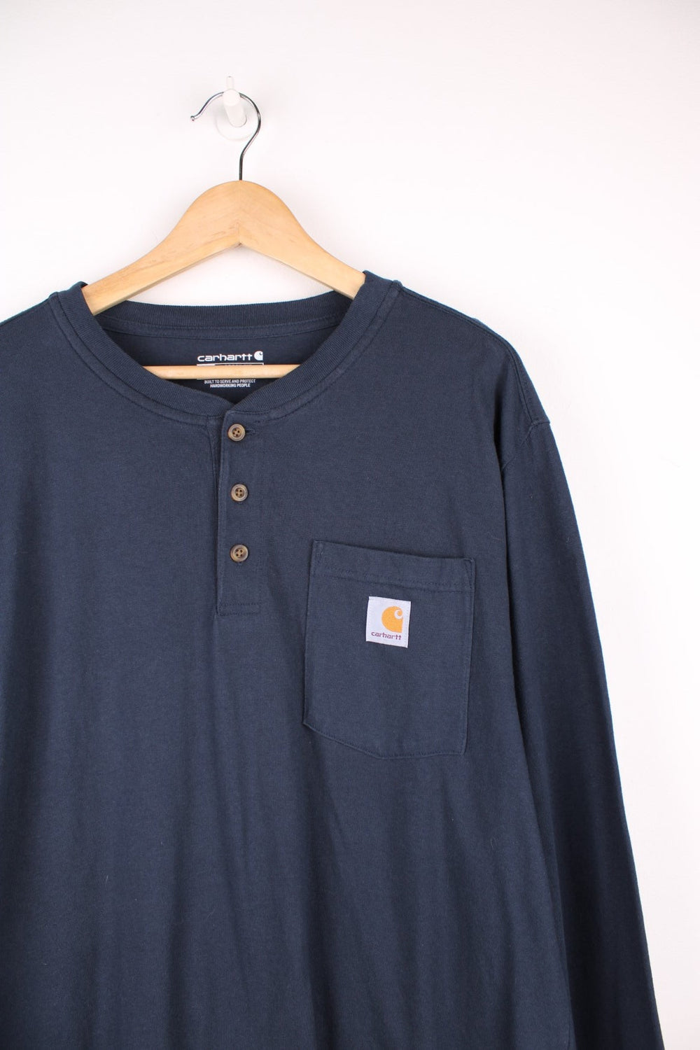 Carhartt navy blue long sleeve cotton t-shirt. Features three button fastening and signature logo on the chest pocket 