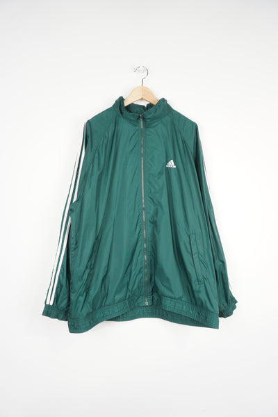 Vintage 1990's green Adidas track jacket features white three stripe details down the arms, embroidered logo on chest and foldaway hood.