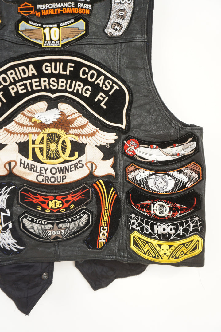 Men's vintage Harley Davidson Owners Group black leather vest with lots of commemorative patches, pins and bike chain details