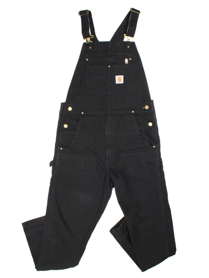 Carhartt Dungarees in black colourway with multiple pockets, adjustable straps, and the logo embroidered on the front.