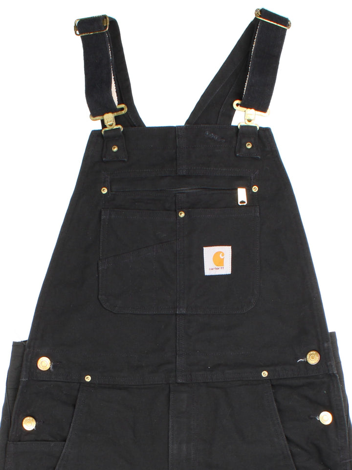 Carhartt Dungarees in black colourway with multiple pockets, adjustable straps, and the logo embroidered on the front.