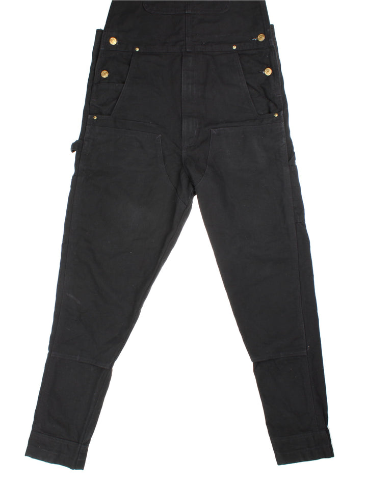 Carhartt Dungarees in black colourway with multiple pockets, adjustable straps, and the logo embroidered on the front.