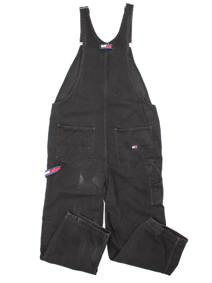 Tommy Hilfiger Dungarees in black colourway with multiple pockets, branded buttons and the logo embroidered on the front/back.