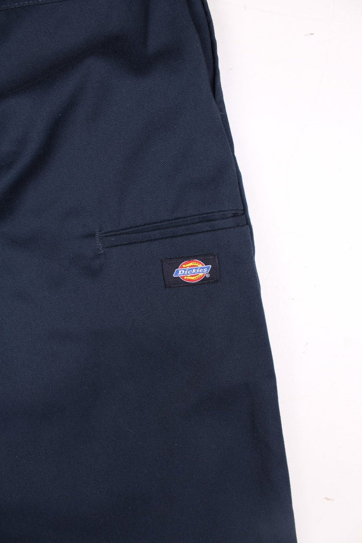 Dickies double-knee work trousers in navy blue with multiple pockets, zip and button closure, and a logo patch on the front.