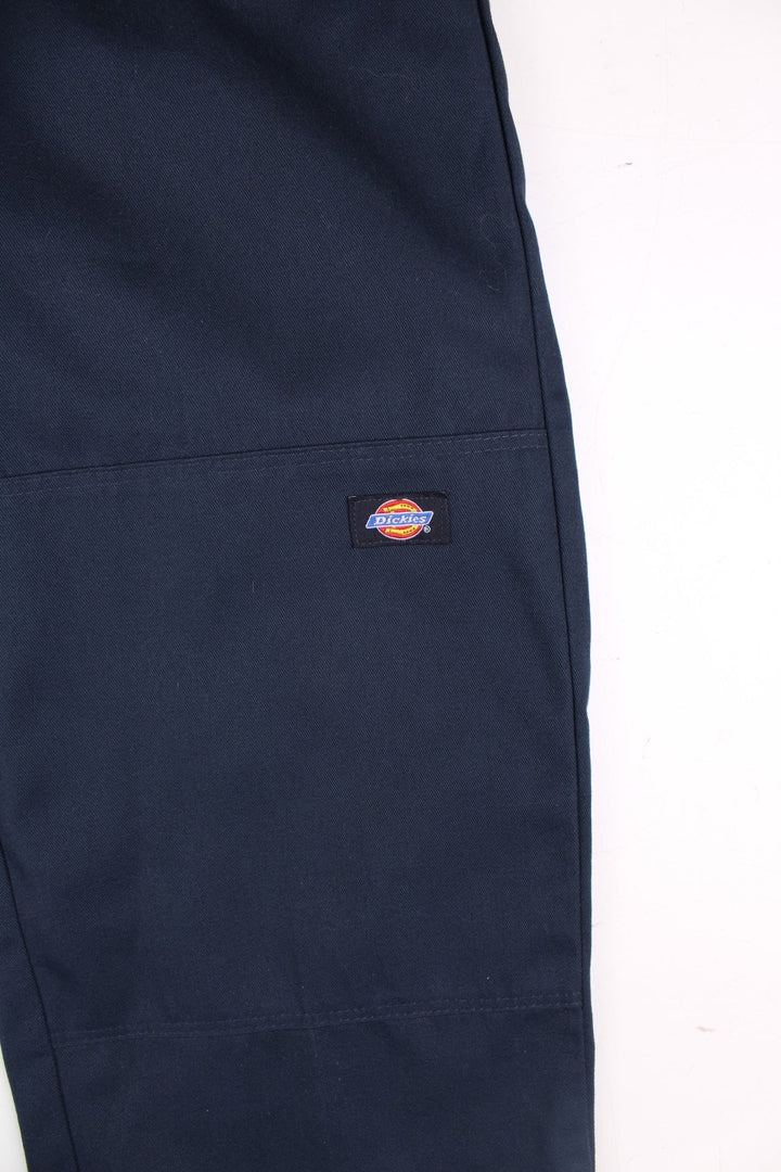 Dickies double-knee work trousers in navy blue with multiple pockets, zip and button closure, and a logo patch on the front.