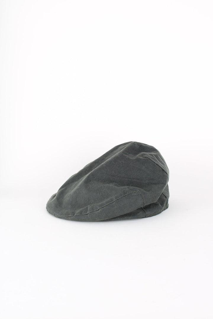 Vintage Barbour Wax Flat Cap in a dark green colourway with tartan lining, and has button closure at the top.