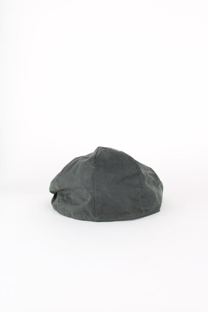 Vintage Barbour Wax Flat Cap in a dark green colourway with tartan lining, and has button closure at the top.