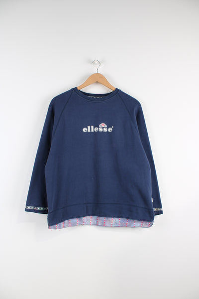 Vintage Ellesse sweatshirt in blue with embroidered logo on the chest and around the cuffs of the arms, also has a tartan pattern stitched into the inside of the sweatshirt at the bottom.