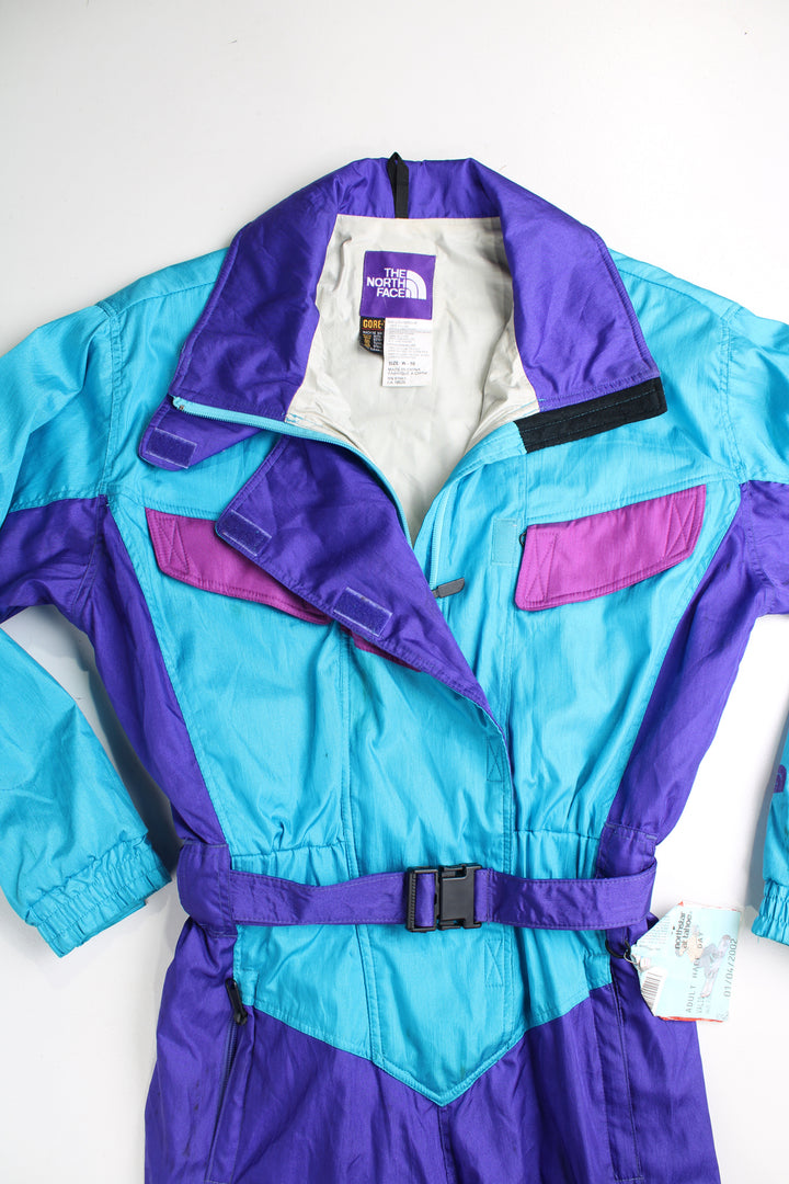 Vintage 90's blue The North Face ski suit. Padded jumpsuit with belt. Closes with a zip/ velcro and has an elasticated waistband at the back. fair condition - Lots of marks throughout, has a old ski pass attached (see photos) Size in Label: Womens 10