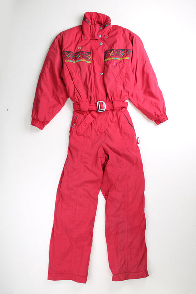 Vintage pink Fila ski suit. Padded jumpsuit with belt. Closes with a zip/ popper buttons and has an elasticated waistband at the back.  good condition - Missing its hood and has a badge on the front that can be removed. Some light marks on the leg cuffs. Size in Label: Womens No Size Label - Measures like a XS