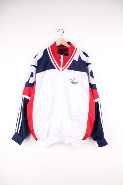 Adidas Tracksuit Jacket in a white, blue and red patterned colourway, zip up with side pockets, has embroidered spell out going around the shoulders as well as logos on the front and back.