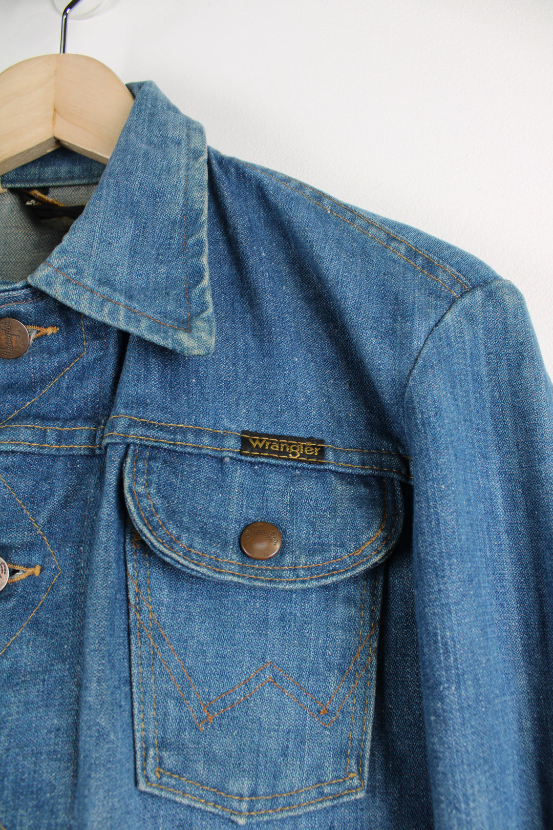 Vintage Wrangler Denim Jacket in a blue colourway with brown cross stitching throughout, button up, multiple pockets, and has logo embroidered on the chest.