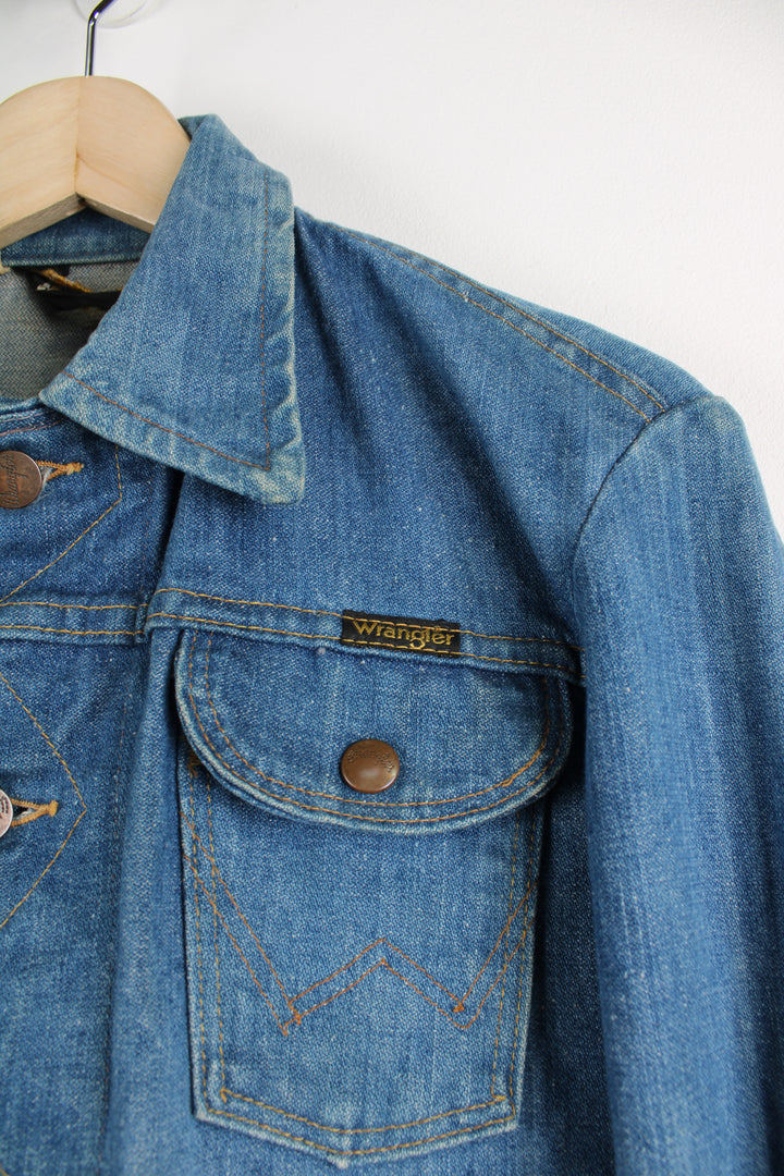 Vintage Wrangler Denim Jacket in a blue colourway with brown cross stitching throughout, button up, multiple pockets, and has logo embroidered on the chest.