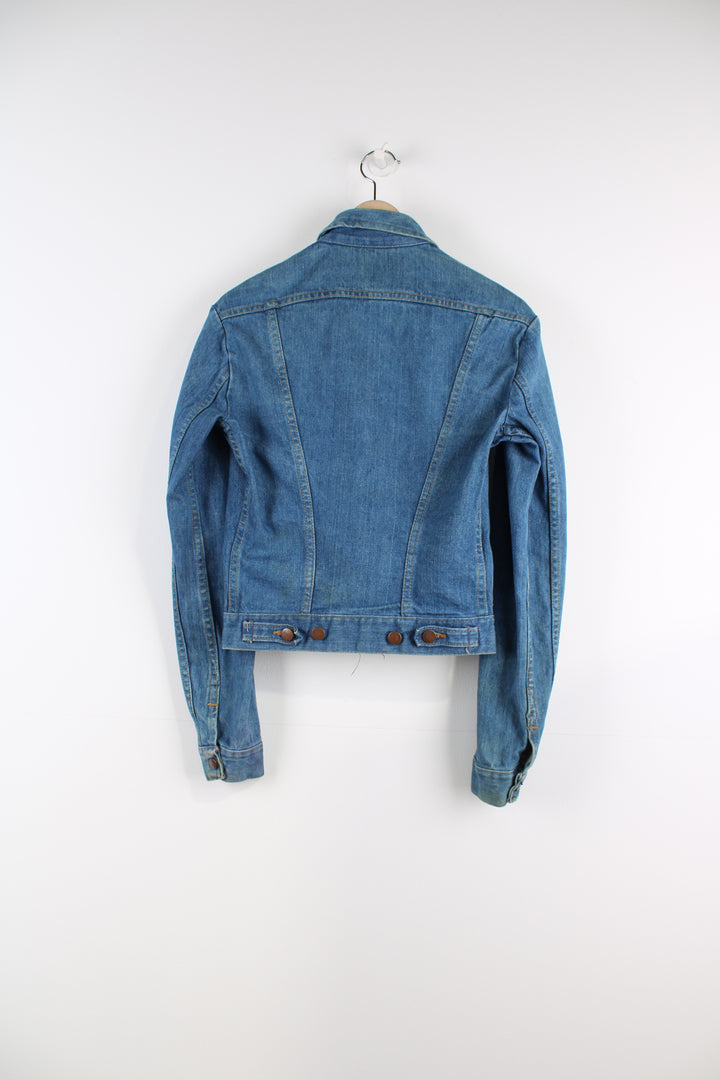 Vintage Wrangler Denim Jacket in a blue colourway with brown cross stitching throughout, button up, multiple pockets, and has logo embroidered on the chest.